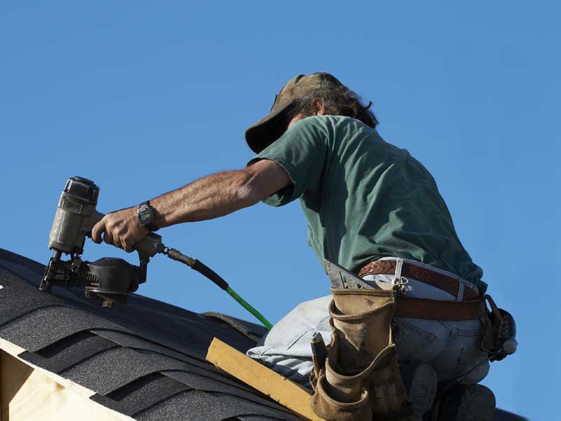 Close up of worker installing new shingles on a residential roof with a nail gun