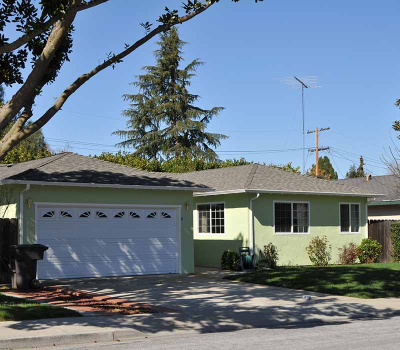 Small, light green residential home with a gray shingle roof